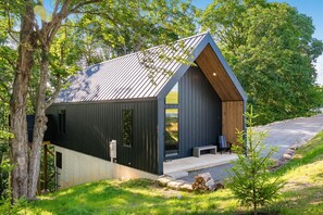 A modern cabin with a sloped roof, large windows, and a wooden porch. - Luxury Couples Cabin in Hocking Hills, Ohio with private hot tub and outdoor fireplace on covered private balcony with forest views. (New Plymouth)