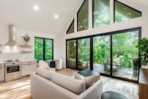 A modern kitchen with built-in appliances, a dining area with a round table and chairs, and large sliding glass doors leading to an outdoor deck. - Luxury Couples Cabin in Hocking Hills, Ohio with private hot tub and outdoor fireplace on covered private balcony with forest views. (New Plymouth)