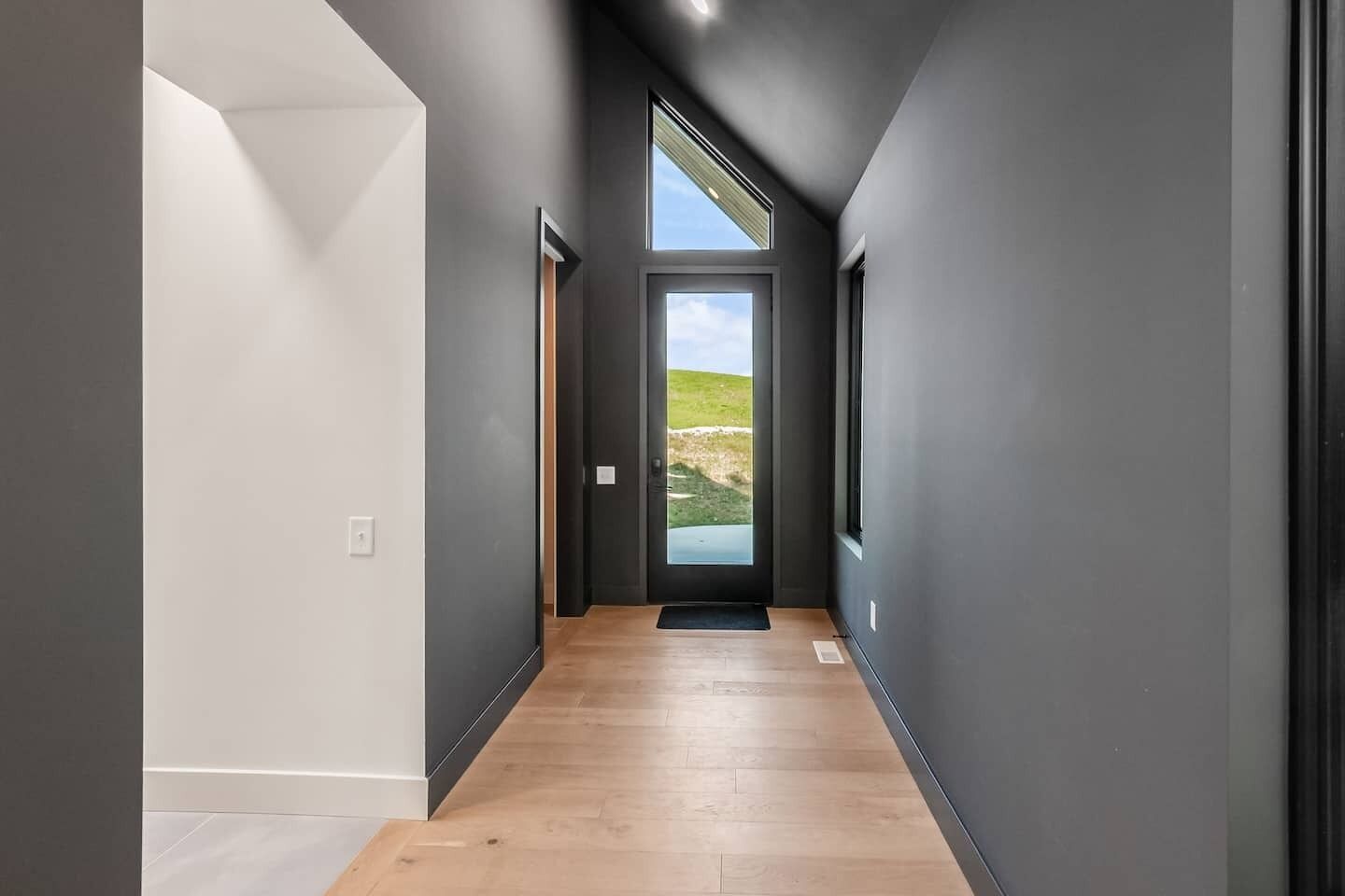 Un couloir doté d’un plancher en bois, de murs gris et d’une porte donnant sur un paysage verdoyant.