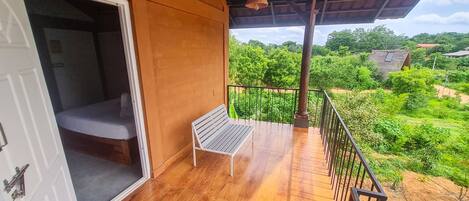 Un balcón con piso de madera, una banca de metal y vistas a un paisaje verde exuberante.