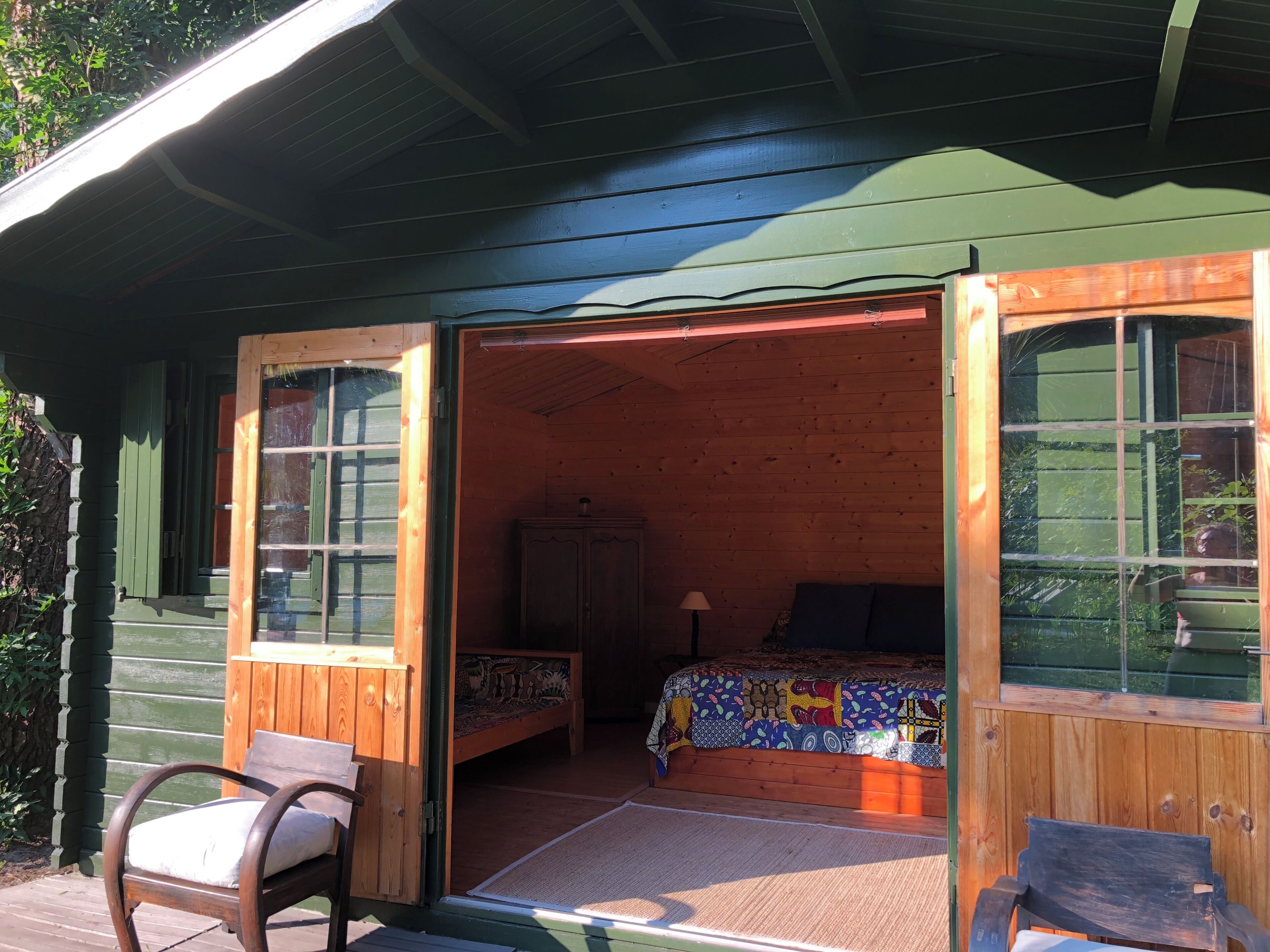 A wooden cabin with an open door leading to a bedroom with a bed and a nightstand.