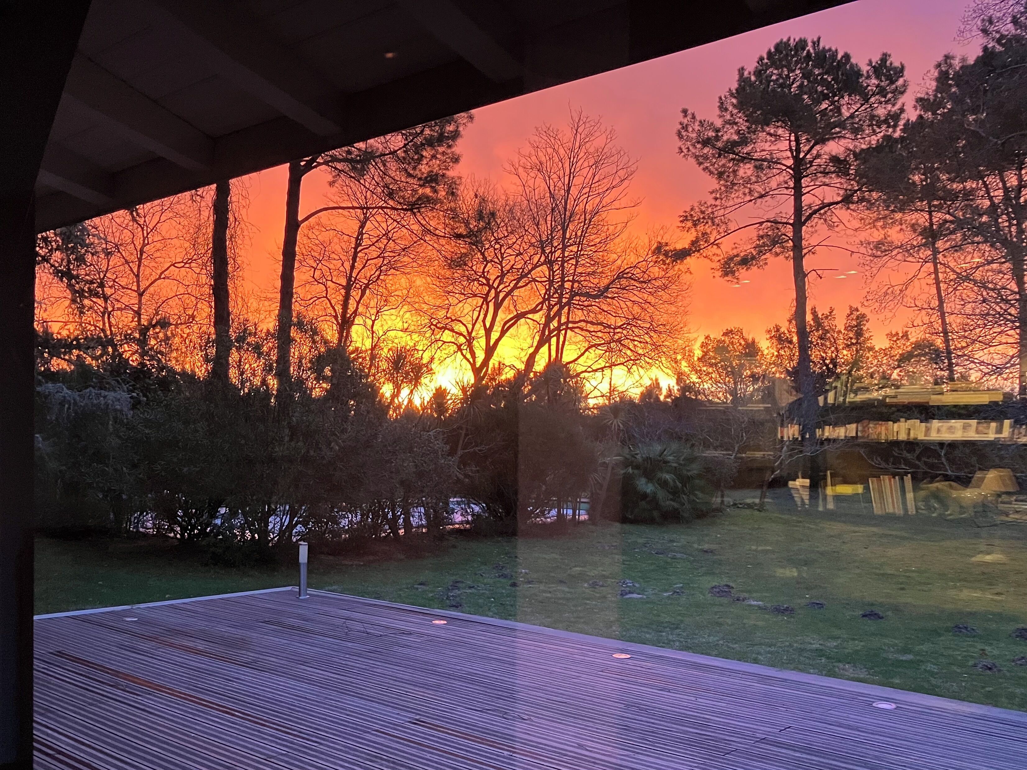 A wooden deck with a view of a sunset over trees.