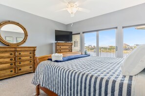 A bedroom with a bed, a dresser, a television, and a large window with a view. - Bay Views & Breezes  ~ Beach & Bay! (Pensacola Beach)