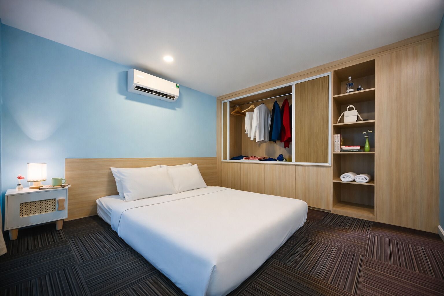 A hotel room with a bed, a nightstand, a wardrobe, and an air conditioning unit.