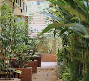 A narrow pathway flanked by potted plants and brick planters, leading to a building with a wooden fence and greenery in the background. - MyRoom An Viên - District 1 (Ho Chi Minh City)