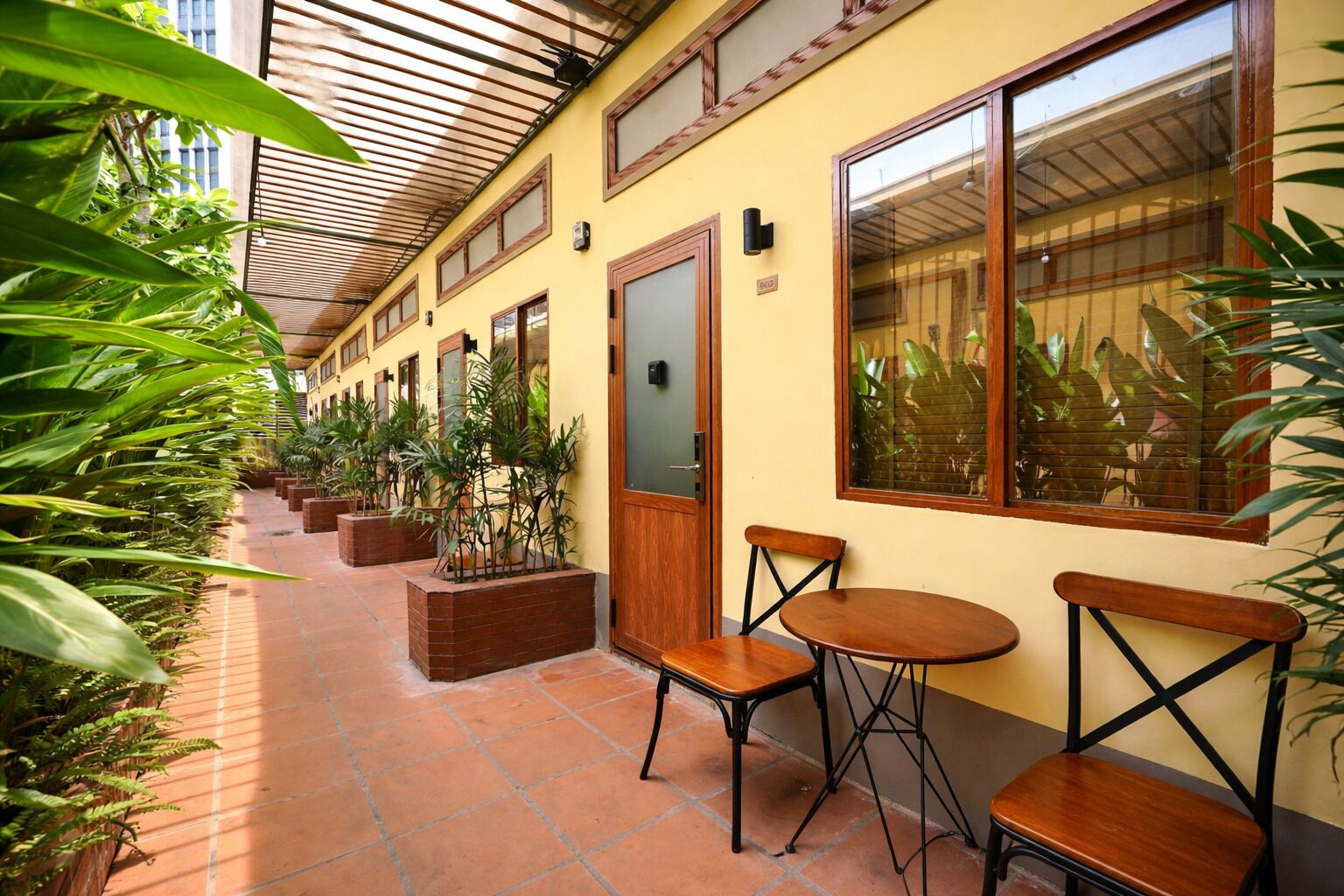 A corridor with potted plants, wooden benches, and a tiled floor.