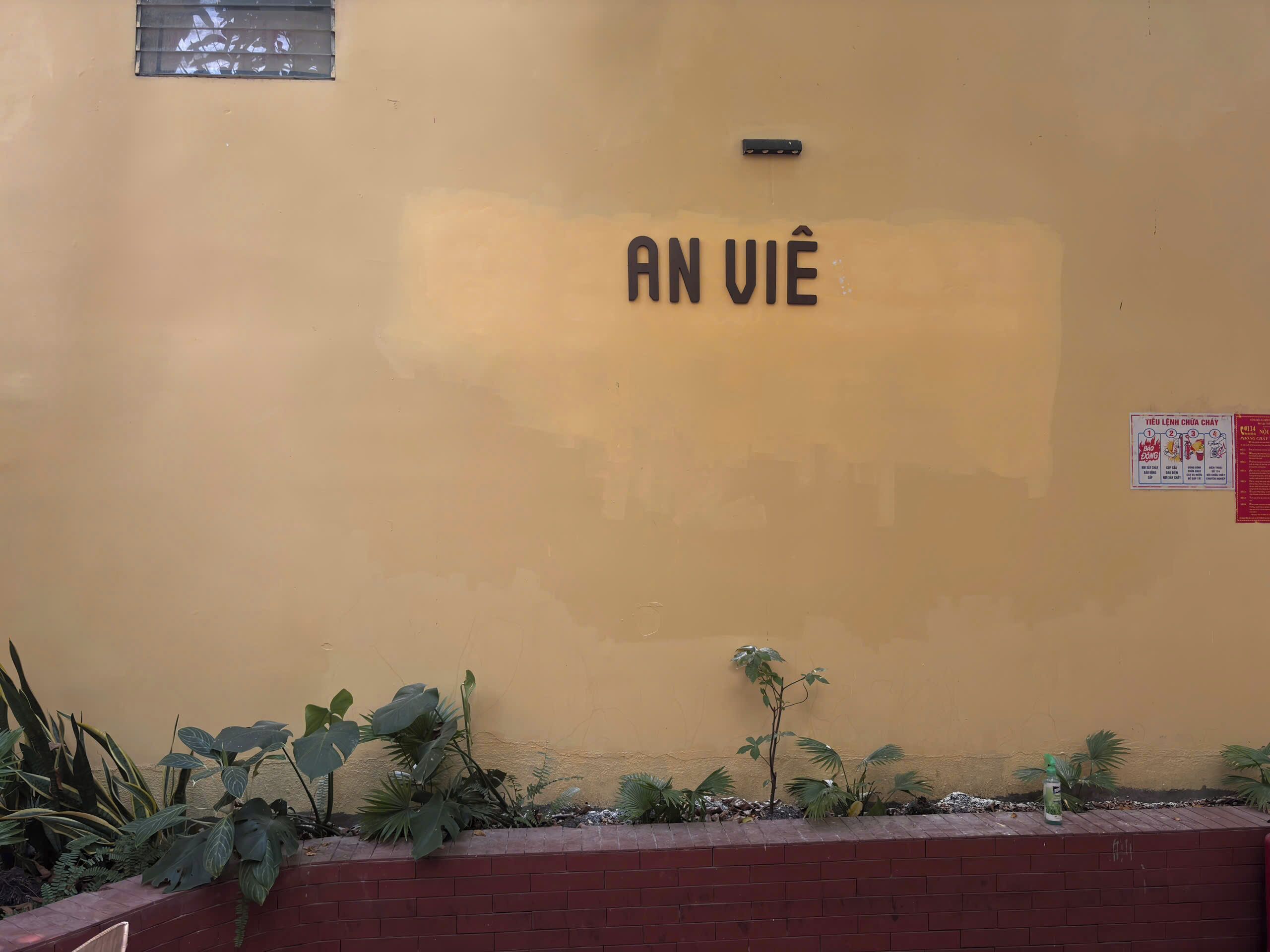 A yellow wall with the text 'AN VIÊ' and a small sign with text and images.