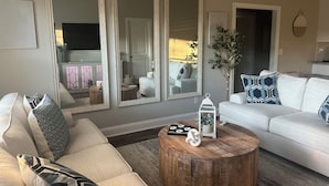 Ein Wohnzimmer mit einem weißen Sofa, einem runden Holztisch und drei großen Spiegeln an der Wand.