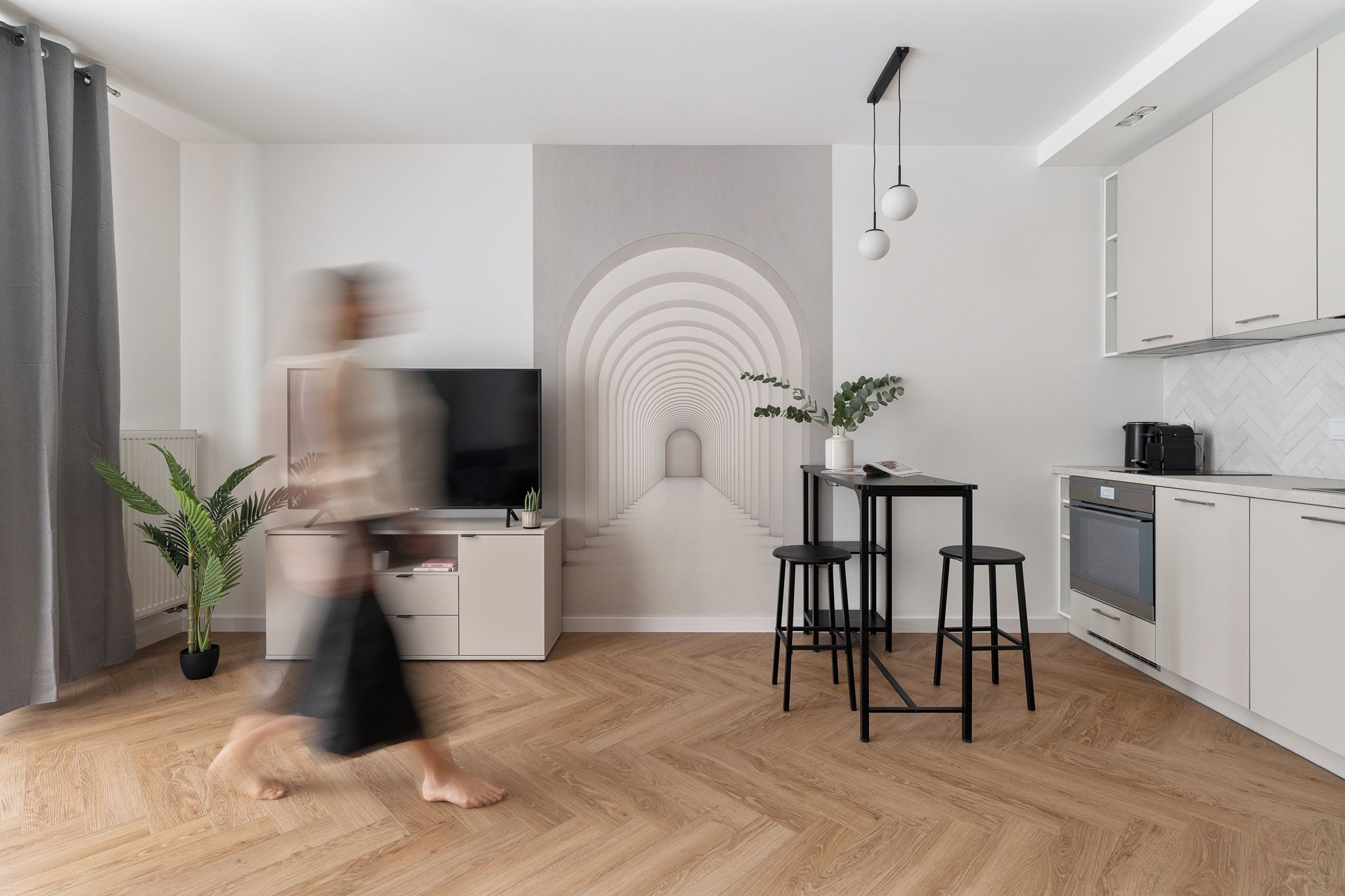 Ein modernes Wohnzimmer mit Fernseher, eine Essecke mit Hocker und eine Küche mit Schränken.
