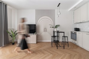 A modern living room with a TV, a dining area with stools, and a kitchen with cabinets. - Towarowa Square & Parking by Downtown Apartments (Warszawa)