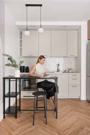 A modern kitchen with a central island, a black metal table, and a person reading a magazine. - Towarowa Square & Parking by Downtown Apartments (Warszawa)