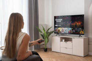 Una persona sentada en una sala de estar moderna con un televisor de pantalla plana mostrando una serie de Netflix.