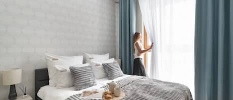 A modern bedroom with a bed, pillows, a bedside table with a lamp, and a window with curtains.
