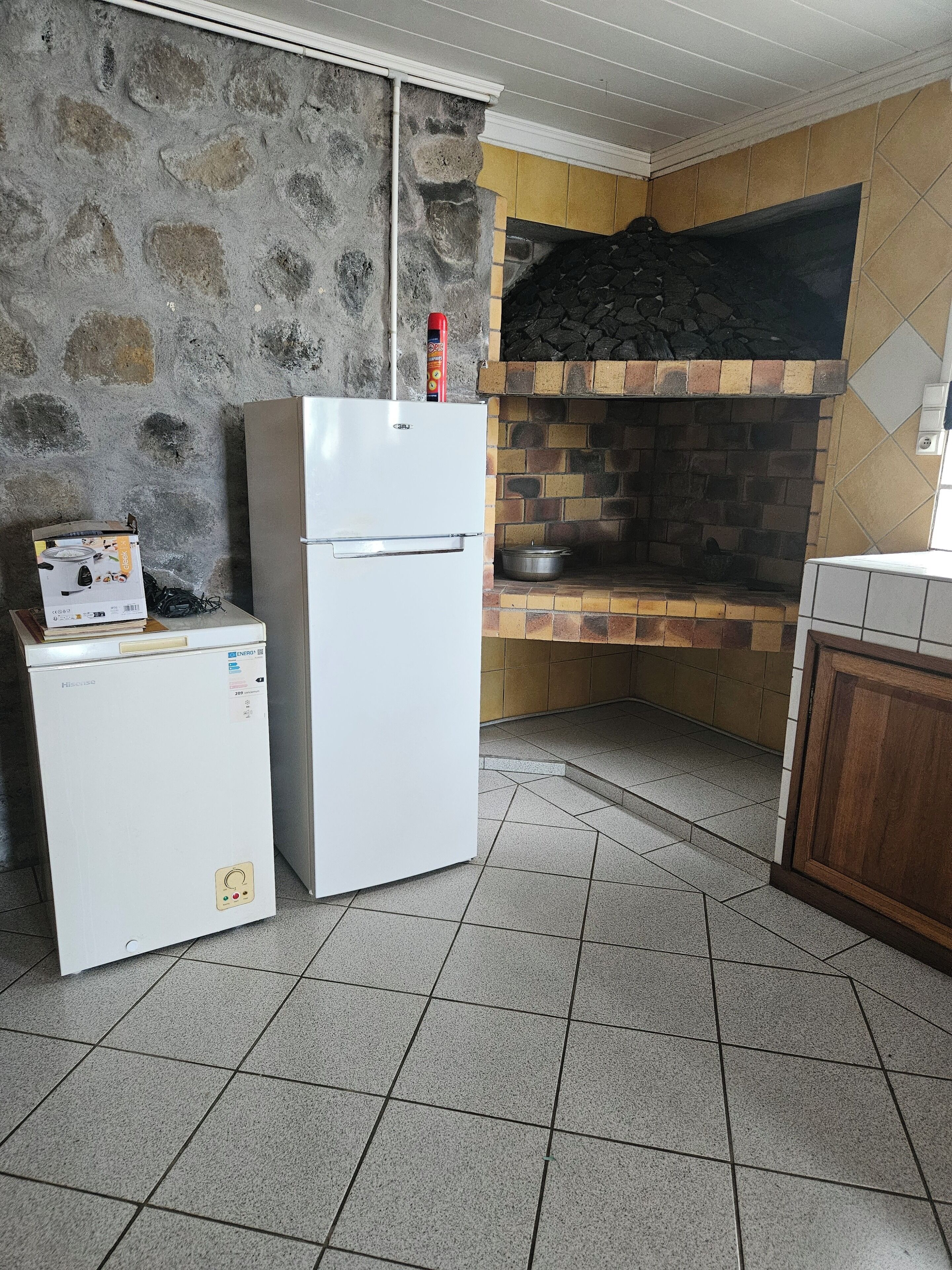 Een keuken met een stenen muur, een witte koelkast, een kleine wasmachine en een bakoven.