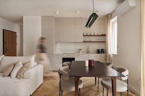Un salon moderne comprenant un canapé, une table à manger et un coin cuisine avec des placards et une machine à café.