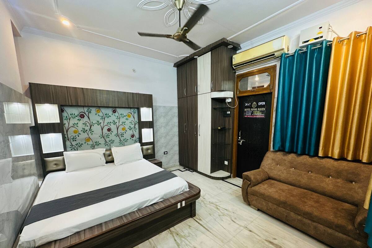 A hotel room with a bed, a sofa, a ceiling fan, a wardrobe, and a door with a sign.