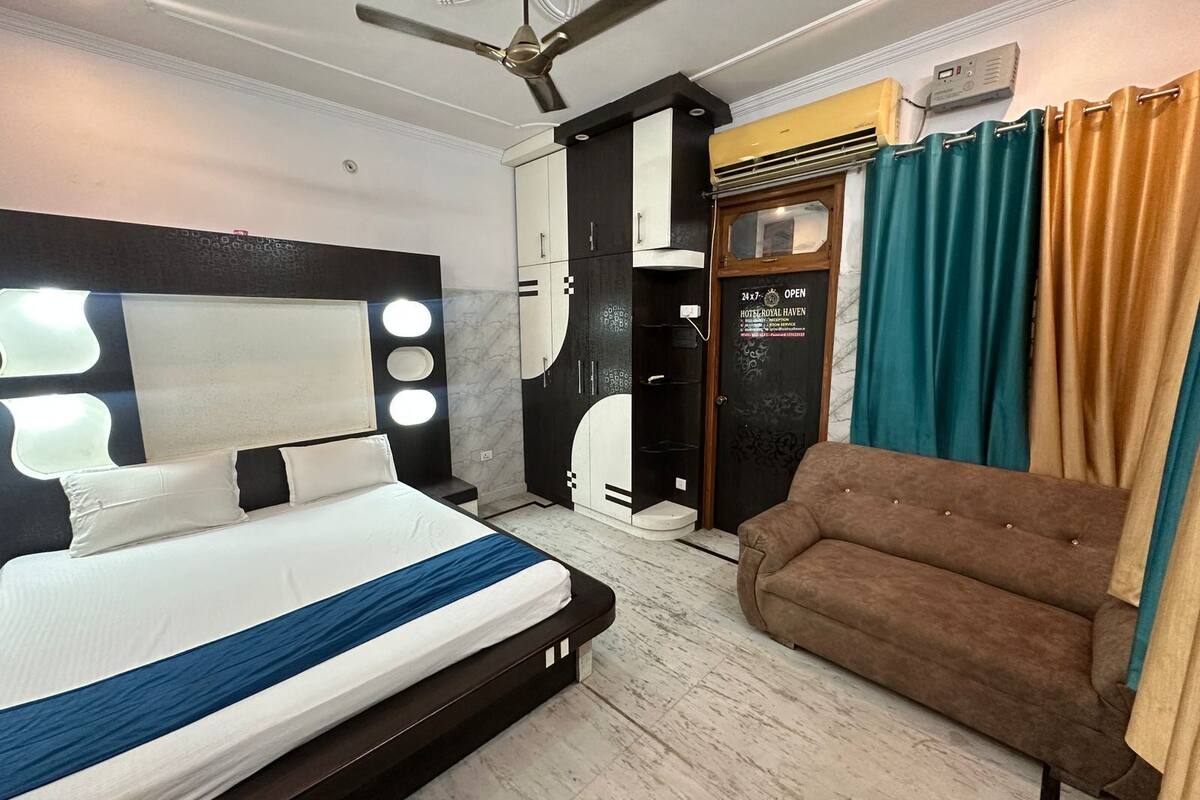 A hotel room with a bed, a ceiling fan, a wardrobe, a sofa, and a door with a sign.