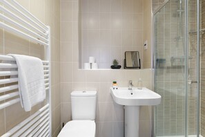 Een badkamer met een wit toilet, een wastafel, een glazen douchecabine en een handdoekrek met een handdoek.