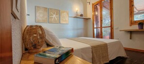 Un dormitorio con cama, una mesita de noche con un libro, una cesta de mimbre y decoración en la pared.