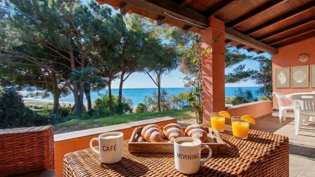 A breakfast setup with croissants, coffee, and orange juice on a wicker table with a view of the sea and trees. - La Villa sul Mare - Direct beach front access (Geremeas)