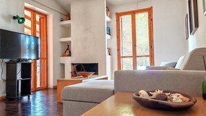 A living room with a television, a fireplace, a sofa, and a table with a bowl of seashells. - La Villa sul Mare - Direct beach front access (Geremeas)