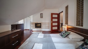 A bedroom with a bed, bedside tables, a wooden dresser, a fireplace, and a large window with decorative glass panels.