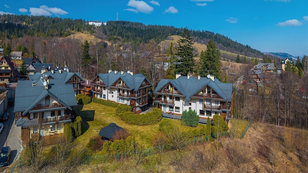 A cluster of chalet-style buildings with multiple balconies, surrounded by a forested hillside.