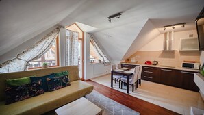 A cozy attic bedroom with a sofa, a dining table, and a kitchen area.