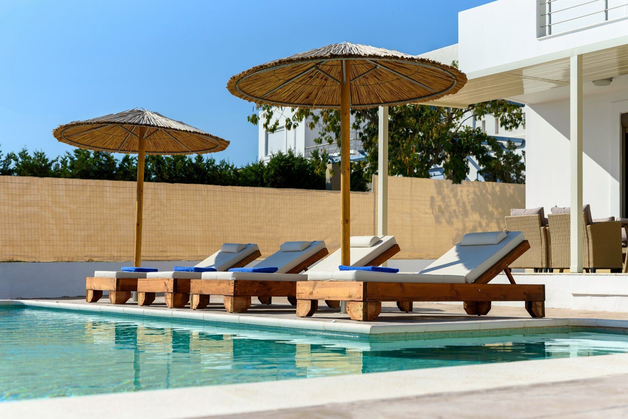 Un área de piscina con sillones de descanso y sombrillas de paja.