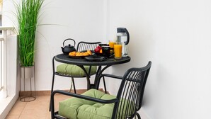 En liten balkong med ett runt bord, två stolar, en krukväxt, en vattenkokare, en kaffekopp och ett glas apelsinjuice.