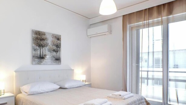 Una camera d'albergo con un letto, un quadro, un condizionatore d'aria e una finestra con tende.