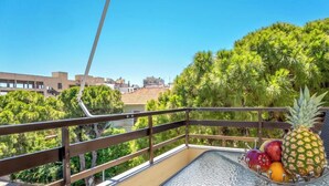 Un balcone con ringhiera in metallo, un tavolo con una ciotola di frutta e vista su edifici e alberi.