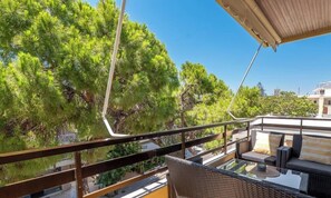 A balcony with a glass table and wicker furniture, overlooking a lush green landscape and a building in the background. - Rhodes Heart Suite, Apartment (Rhodes)