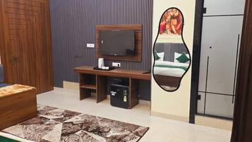 Een hotelkamer met een houten deur, een televisie op een houten standaard, een bed met een groene spreidek en een tapijt met een patroon, en een spiegel aan de muur.