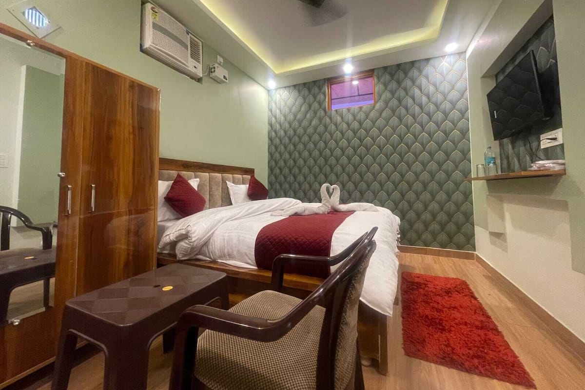 A hotel room with a bed, a desk, a chair, a TV, and a red rug.