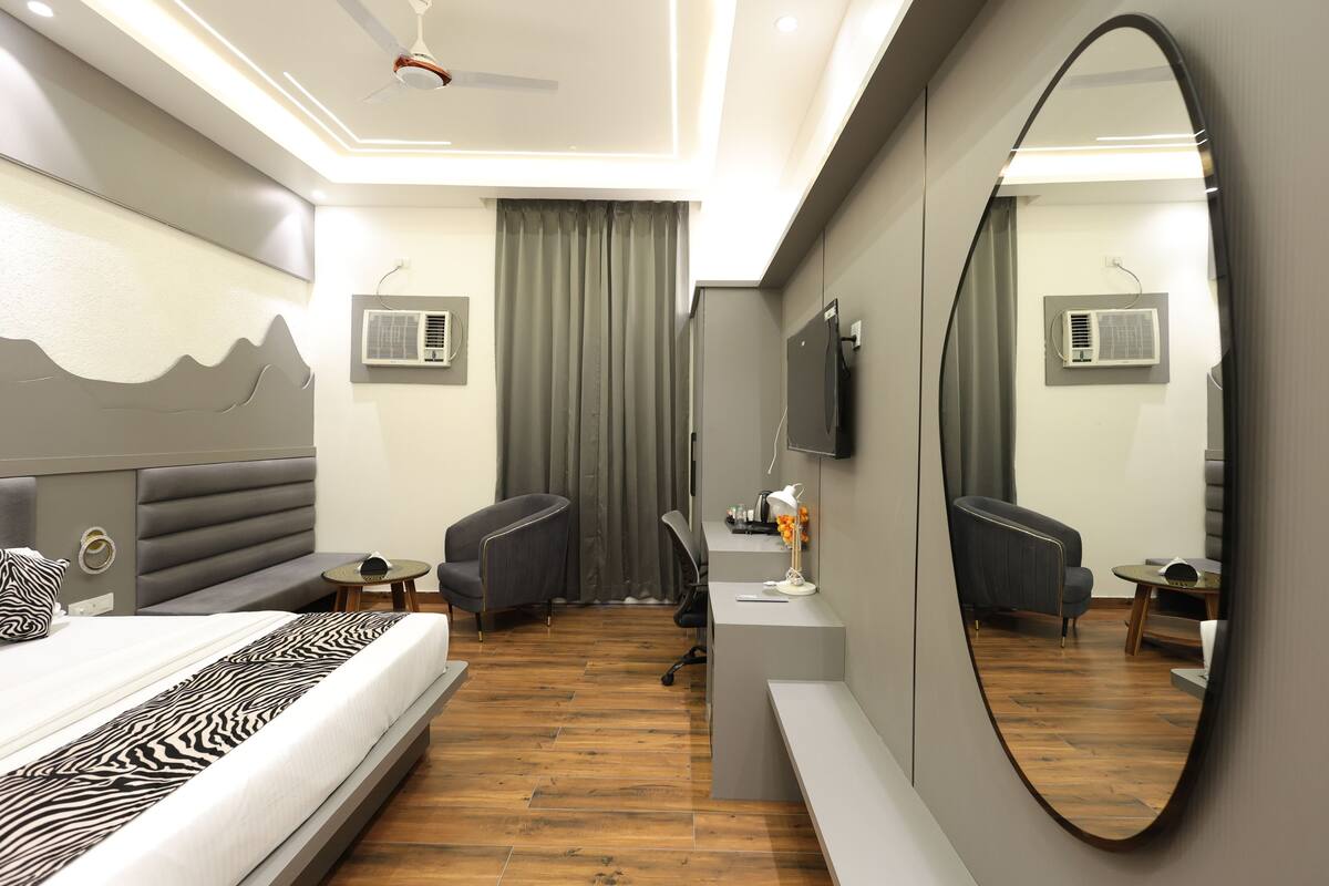 A modern hotel room with a bed, a desk, a chair, a mirror, and a ceiling fan.