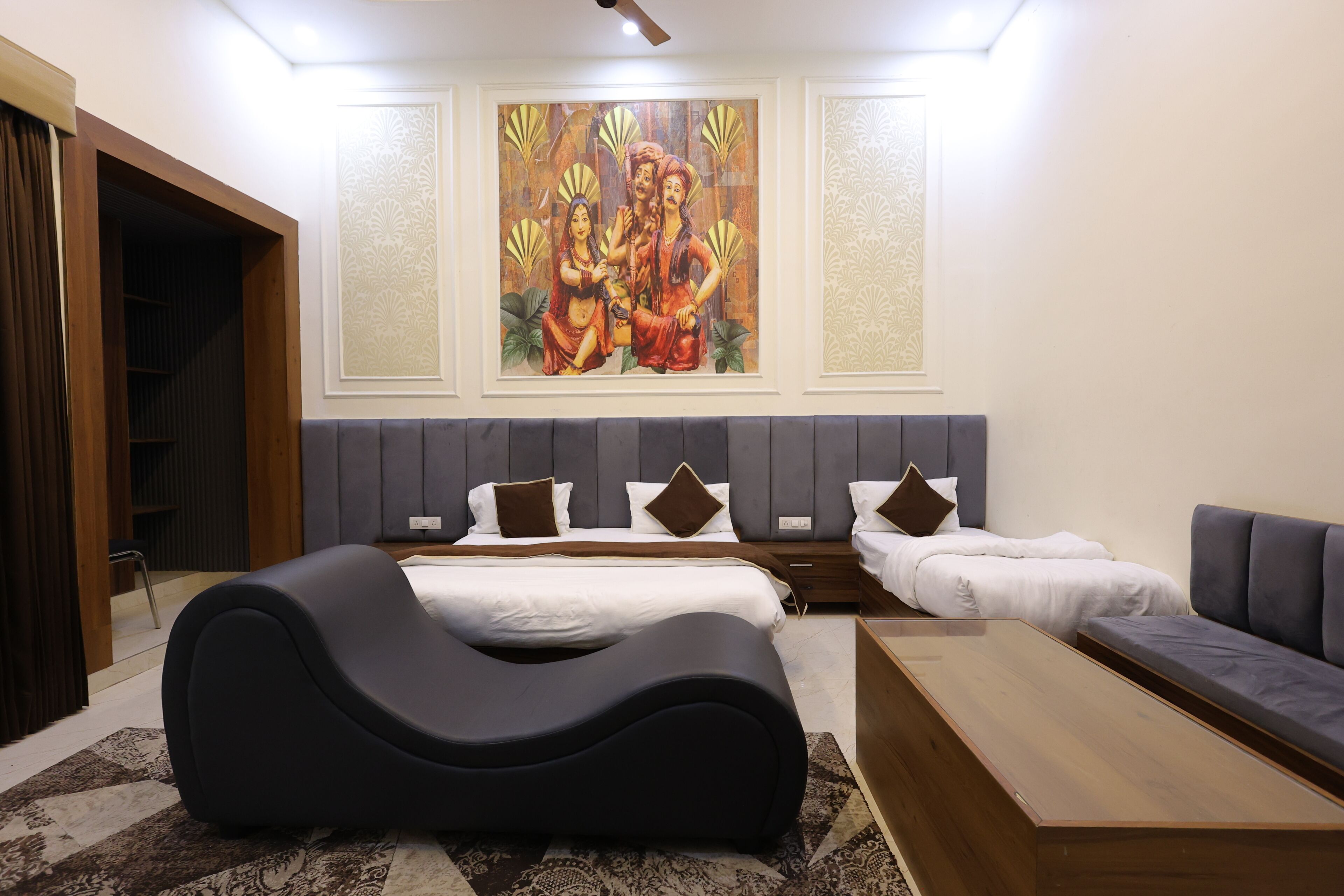 A modern hotel room with a large bed, a sofa, a unique black chair, and a painting on the wall.