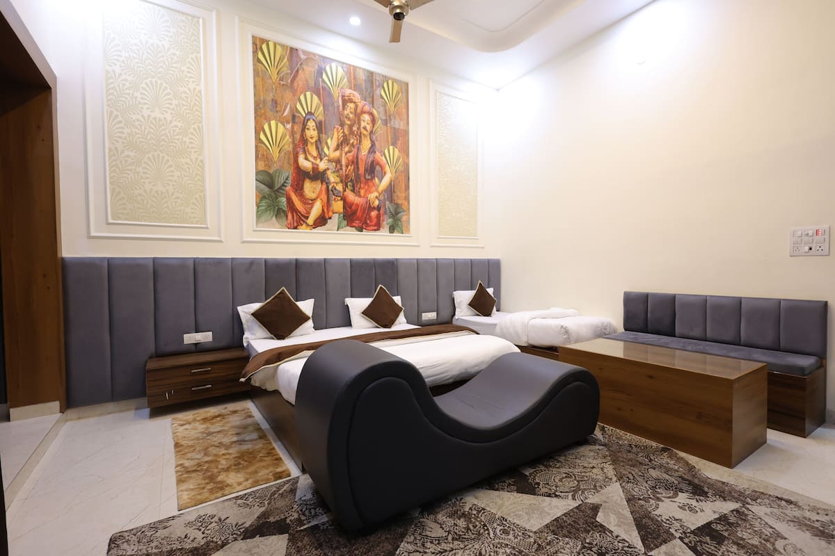 A modern hotel room with a large bed, a sofa, a desk, and a painting on the wall.