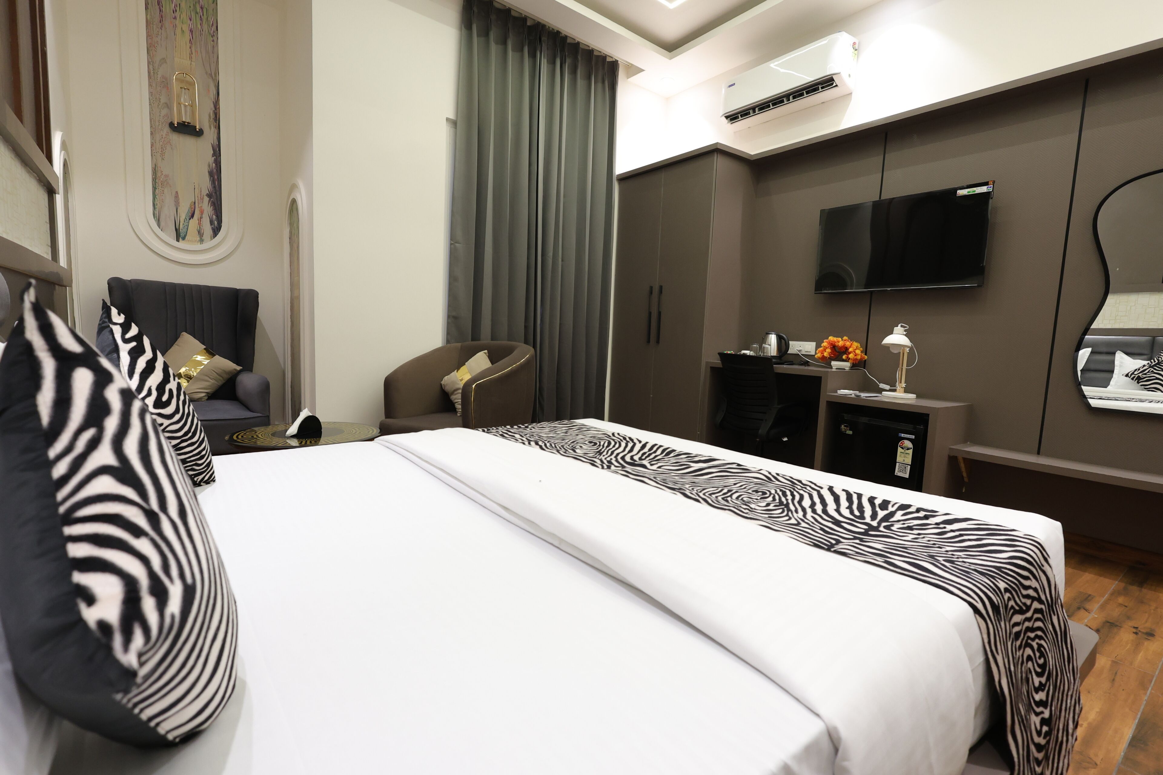 A modern hotel room with a large bed, a flat-screen TV, a desk with a lamp, and a wardrobe.