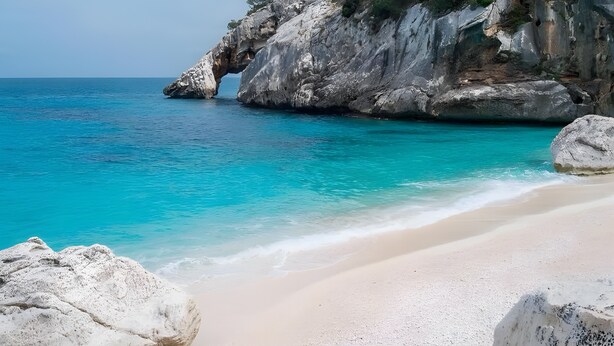 Una playa con agua turquesa cristalina, un acantilado rocoso y una gran formación rocosa.