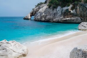 Una playa con agua turquesa cristalina, un acantilado rocoso y una gran formación rocosa.