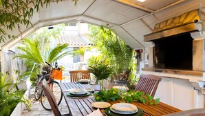 Un área de comedor al aire libre con una mesa preparada para dos personas, rodeada de macetas con plantas y una bicicleta.