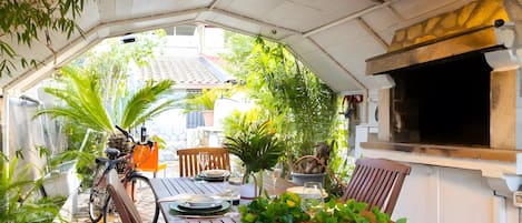 An outdoor dining area with a table set for two, surrounded by potted plants and a bicycle.