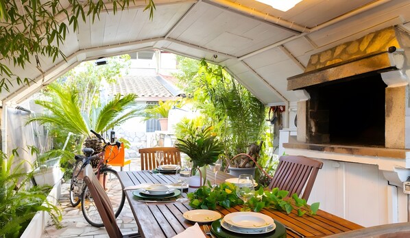 Un área de comedor al aire libre con una mesa preparada para dos personas, rodeada de macetas con plantas y una bicicleta.