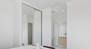 Un dormitorio con un espejo grande, una cama, un armario y un baño con ducha.