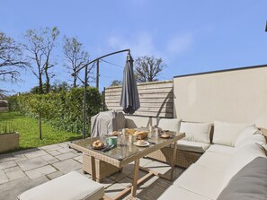 Un patio al aire libre con mobiliario de mimbre, una mesa dispuesta con comida y bebidas, y una zona techada.