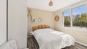 A bedroom with a large bed, a window with a view of trees, a wooden headboard, and a small bedside table. - Beach 300m away, house 8 adults and 2 children (La Plaine-sur-Mer)