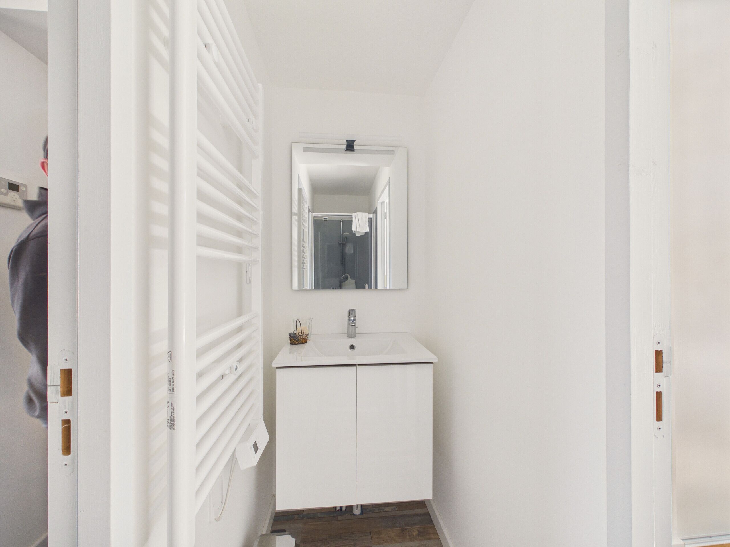 A white bathroom with a mirror, sink, and radiator.