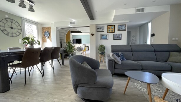A modern living room with a grey sofa, a dining area with chairs, and a kitchen in the background. - Beach 300m away, house 8 adults and 2 children (La Plaine-sur-Mer)