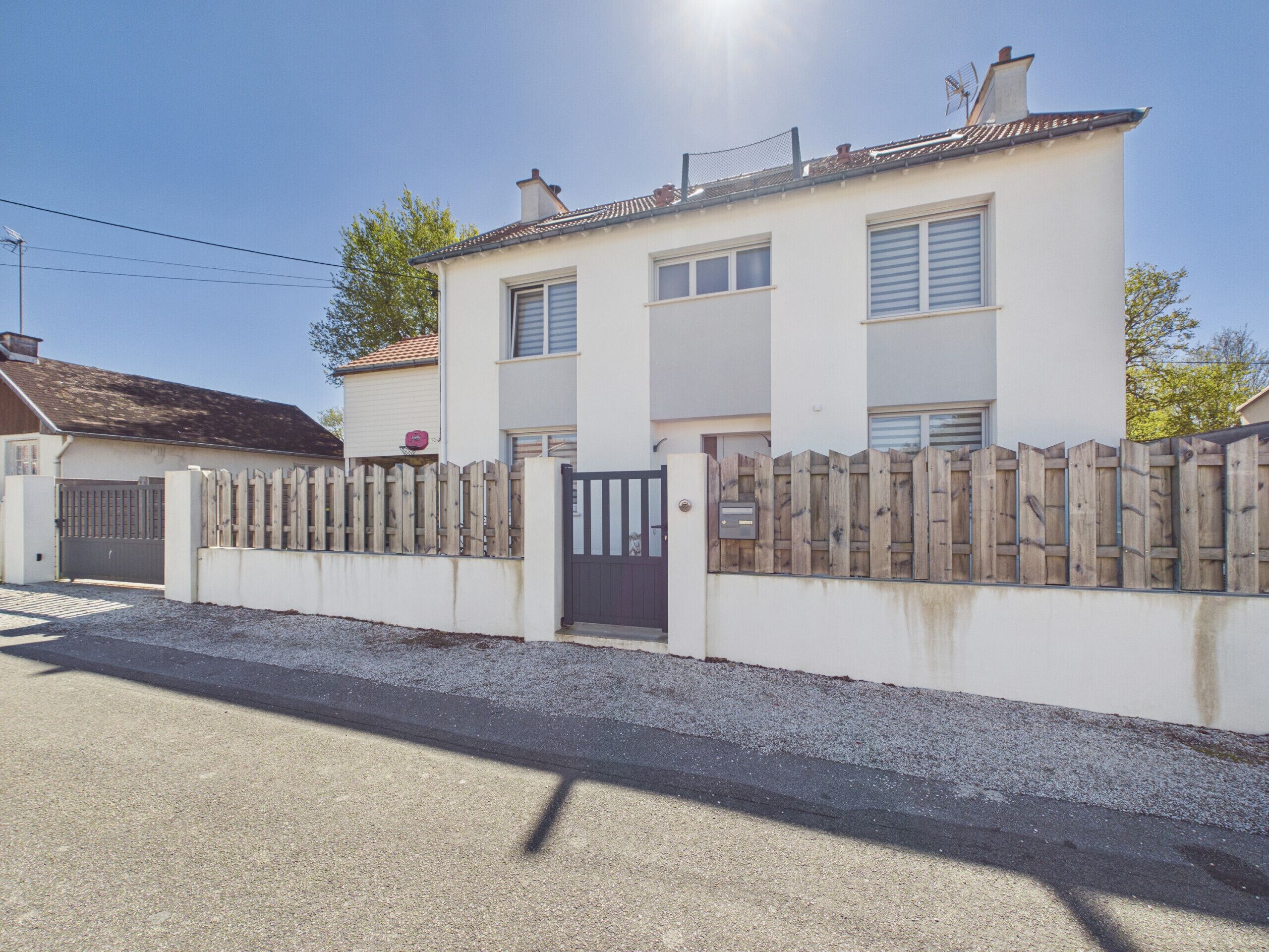 A two-story house with a gated driveway, a wooden fence, and a clear sky.